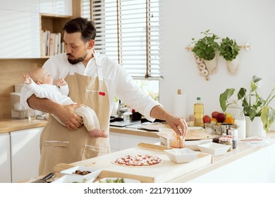 Handsome Father Holding Baby Looking At Dressing Homemade Pizza Preparing Dinner For Family.