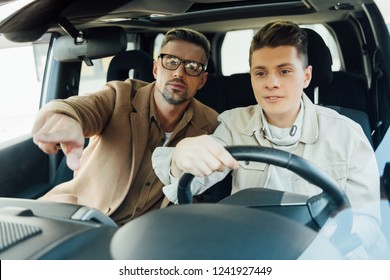 Handsome Father Pointing On Something While Teaching Teen Son Driving Car