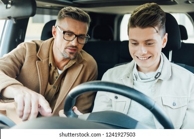 Handsome Father Pointing On Something While Teaching Smiling Teen Son Driving Car