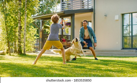 Handsome Father And Son Play Catch With Loyal Family Friend Golden Retriever Dog. Family Spending Time Together Training Dog. Sunny Day Idyllic Suburban Home Backyard.