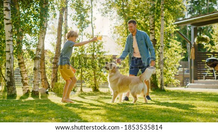 Handsome Father and Son Spend Quality Family Time Together, Play Soccer with Football, Passing to Each other, and Having Fun. Sunny Day Idyllic Suburban Home Backyard with Loyal Golden Retriever Dog
