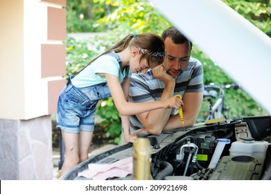 Handsome father teaching his school age daughter to change motor oil in there family car. 
