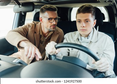 Handsome Father Teaching Teen Son Driving Car And Pointing On Something