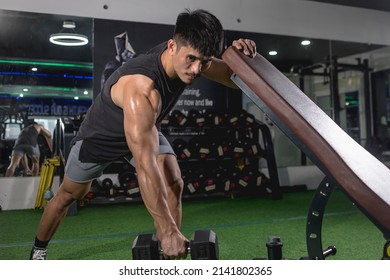 A Handsome And Fit Asian Guy Does One-arm Dumbbell Rows While Leaning On An Incline Bench. Performing Negative Reps. Back Exercise Variation. Weight And Resistance Training At The Gym.