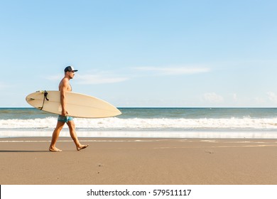 Handsome fit man walk with white blank surfboard wait for wave to surf spot at sea ocean beach. View from side. Concept of sport, fitness, freedom, happiness, new modern life, hipster, generation Y. - Powered by Shutterstock