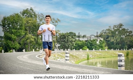 Handsome and fit millennial Asian man in sportswear running or jogging on the side path along the beautiful lake. Healthy lifestyle concept