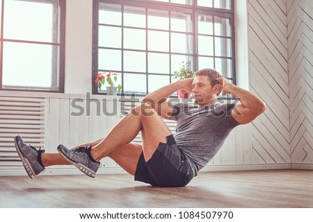 Handsome fitness man in a t-shirt and shorts doing abdominal exercises on floor at home.