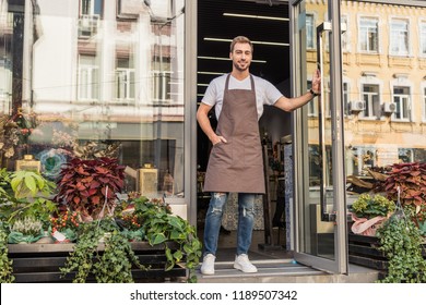 Handsome Florist In Apron Opening Door Of Flower Shop