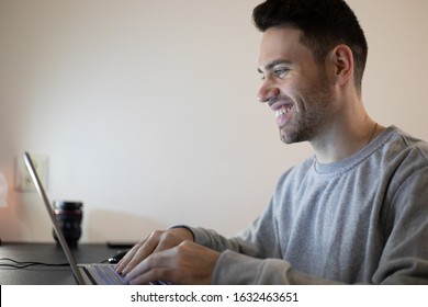 Handsome And Focused Young Man With A Genuine Smile Working On His Laptop From Home. 