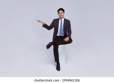 Handsome and friendly face asian businessman smile in formal suit sitting on chair points his hands to presented on white background studio shot. - Shutterstock ID 1994041106