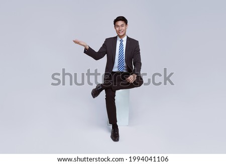 Handsome and friendly face asian businessman smile in formal suit sitting on chair points his hands to presented on white background studio shot.