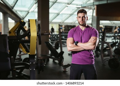 Handsome friendly personal trainer in gym. Young sporty man smiling standing on fitness club background - Powered by Shutterstock