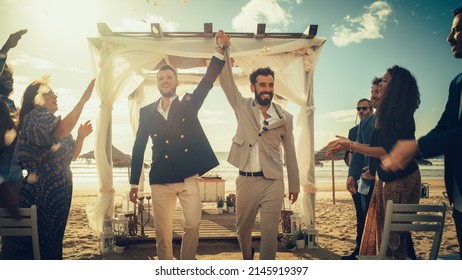 Handsome Gay Couple Walking Up The Aisle At Outdoors Wedding Ceremony Venue Near Sea. Two Happy Men In Love Share Their Big Day With Diverse Multiethnic Friends. Authentic LGBTQ Relationship Goals.