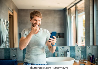 Handsome gentleman cleaning teeth with toothbrush and holding smartphone stock photo - Powered by Shutterstock