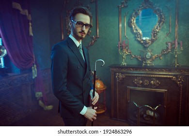 Handsome gentleman in elegant classic suit poses with his walking stick in a luxury apartment. Luxury lifestyle. Men's beauty, fashion.