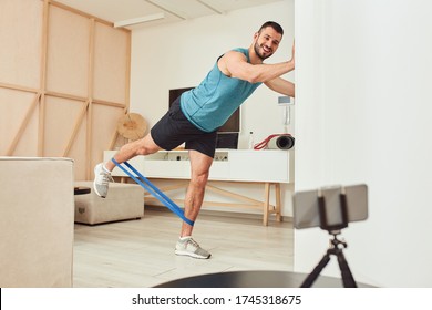 Handsome Gentleman Watching Online Workout On Mobile Phone And Smiling While Having Strength Training At Home