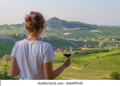 handsome girl holding a glass of red wine looking amazing green vineyards in the italian region of Piedmont, Alba, Barolo, Italy