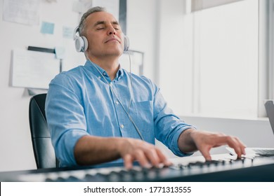 handsome gray-haired smiling man with headphones sits in music studio playing keyboard piano enjoying music looking excited and happy, music record concep, art of composition