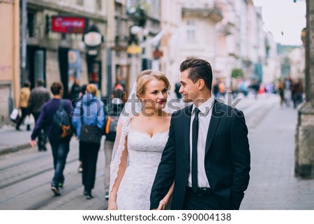 Handsome groom and beautiful bride walking on old european street architecture