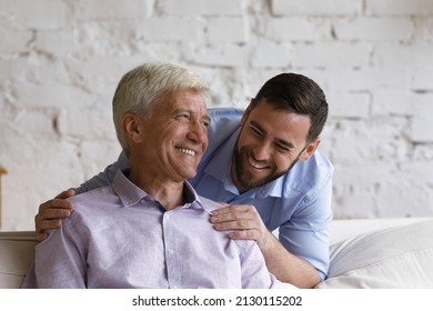 Handsome Grown Up Son Hugs His Elderly Father Feel Happy Laughing Spend Time Together At Home. Understanding, Harmonic Relations Between Two Generation Relatives People. Family Ties And Bond Concept