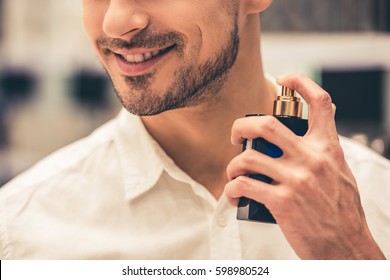 Handsome guy is choosing perfumes and smiling while doing shopping in the mall