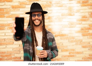 Handsome guy drinking coffee while walking in the street. Modern fashion man using the phone.
