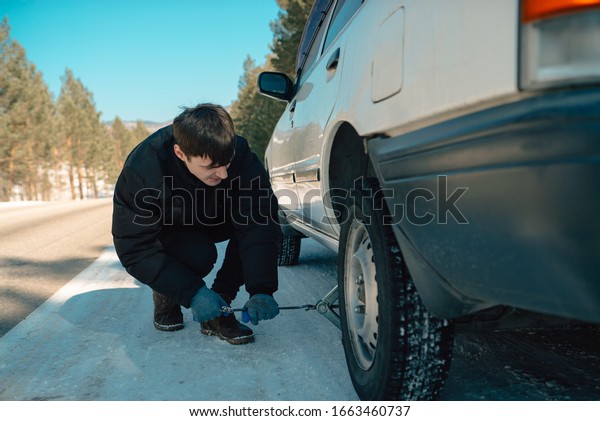 handsome guy fixing a car\'s wheel\
in the sunny winter day on a road in siberia,chanching\
wheel