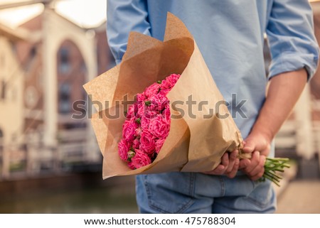 Handsome guy is holding flowers behind his back and waiting for his girlfriend, cropped