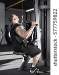 Handsome guy with huge biceps does exercise in the gym. He wears black sleeveless, shorts and sneakers. Shoot from the side. Vertical.