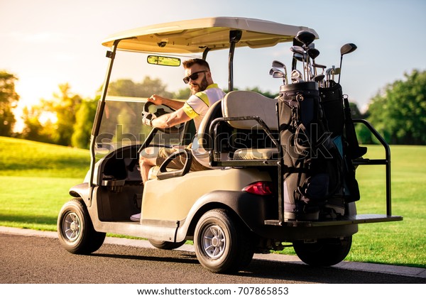 Handsome guy is looking at camera while driving a\
golf cart