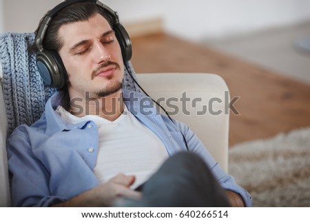 Handsome guy lying on sofa with tablet and headphones