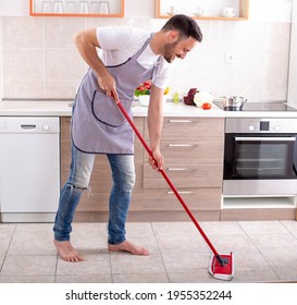 Handsome Guy Mopping Kitchen Floor In Front Of Cabinets And Countertop At Home