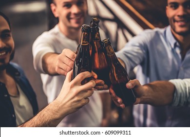 Handsome guys are clinking bottles of beer and smiling while resting in pub - Powered by Shutterstock