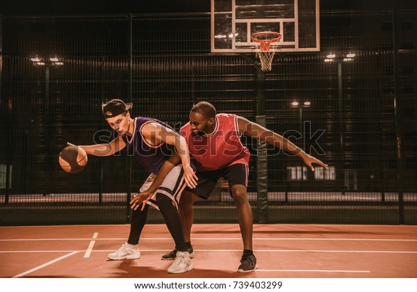 Handsome
guys are playing basketball outdoors at
night