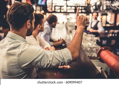 Handsome guys are standing at the bar counter and calling waiter while resting at the pub