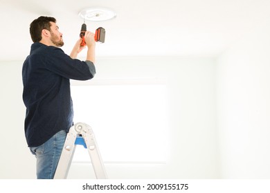 Handsome Handyman Installing A New Light Fixture With An Electric Drill. Young Man In His 30s Doing Home Renovations