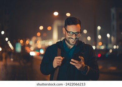 A handsome, happy adult businessman with glasses walking home from work in the evening and typing text messages on his mobile phone. - Powered by Shutterstock