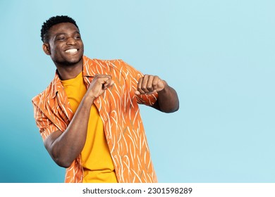 Handsome happy African American man wearing casual clothes dancing, having fun isolated on blue background. Positive lifestyle, summer concept 