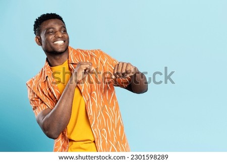 Handsome happy African American man wearing casual clothes dancing, having fun isolated on blue background. Positive lifestyle, summer concept 