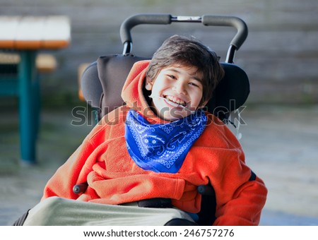 Handsome, happy biracial eight year old boy smiling in wheelchair outdoors