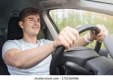 Handsome Happy Cheerful Guy, Driver, Young Possitive Man Driving A Car On Road, Smiling, Holding Steering Wheel Of Automobile. Boy Inside Car Sitting Not Fastened By A Seat Belt. Traffic Violation