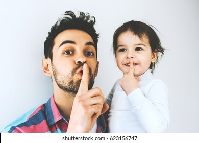 Handsome happy father and beautiful little daughter make quiet gesture, isolated on white background. Fatherhood. Dad show silent gesture with his girl together. Lifestyle family. Secret sign. 