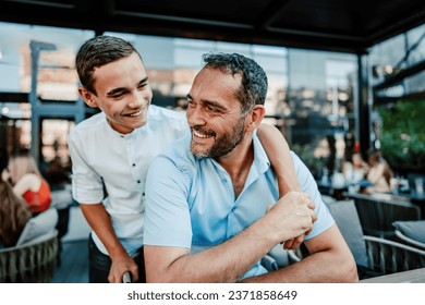 Handsome and happy father and his teenager son sitting in a restaurant and talking. - Powered by Shutterstock