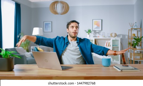 Handsome Happy Man Does Funny Dance Routine While Sitting At His Desk In The Living Room. He Is Doing Arm Wave.