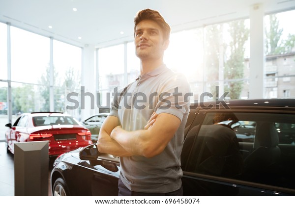 Handsome happy man standing in front of a car at\
the dealership center