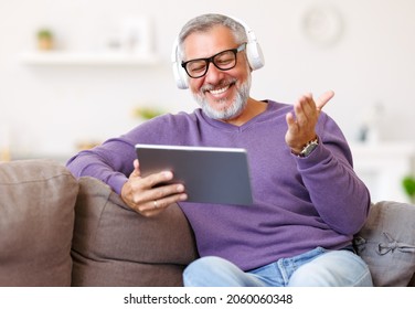 Handsome happy senior man using digital tablet while sitting on sofa at home, cheerful pensioner resting and relaxing in living room with electronic device, chatting with friends in social media - Powered by Shutterstock