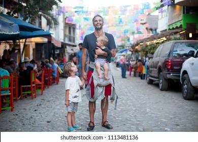 Handsome Happy Smiling Dad With Kids On A Street On Vacation During A Festival In Mexico