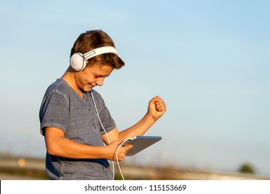 Handsome happy teen boy listening to music on digital tablet outdoors. - Powered by Shutterstock