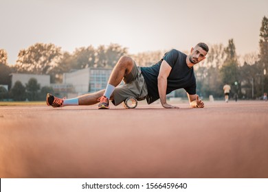 Handsome healthy man doing an exercise outdoors with foam roller on his lower body