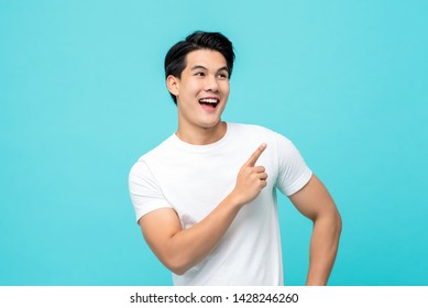 Handsome healthy young Asian man smiling with his finger pointing isolated on light blue studio background